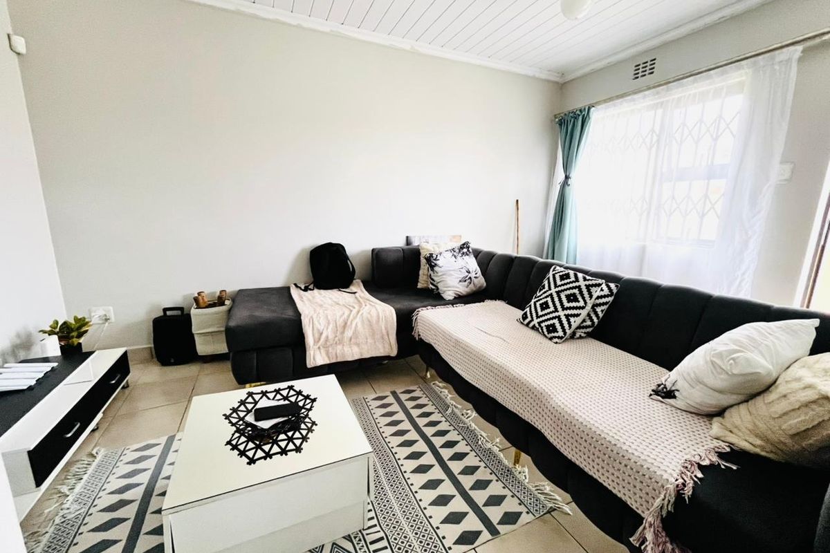 A living room featuring tiled flooring and a timber panelled ceiling, with natural light entering through a window fitted with a security gate.