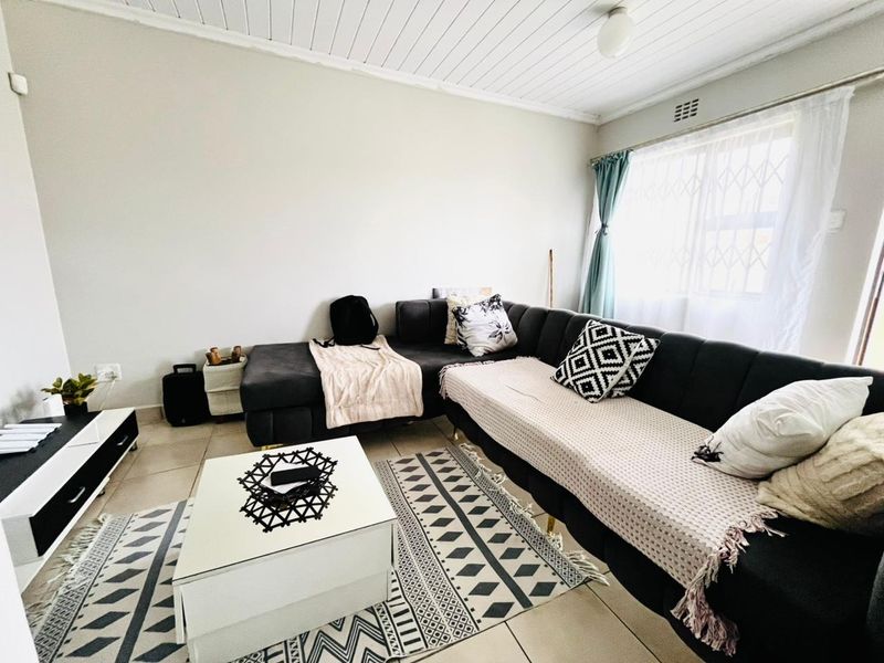 A living room featuring tiled flooring and a timber panelled ceiling, with natural light entering through a window fitted with a security gate.