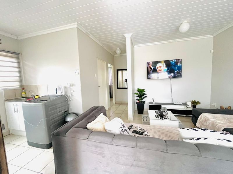 Open-plan living area featuring tiled flooring, a tongue and groove ceiling, and a compact kitchen corner with built-in cabinetry and sink.