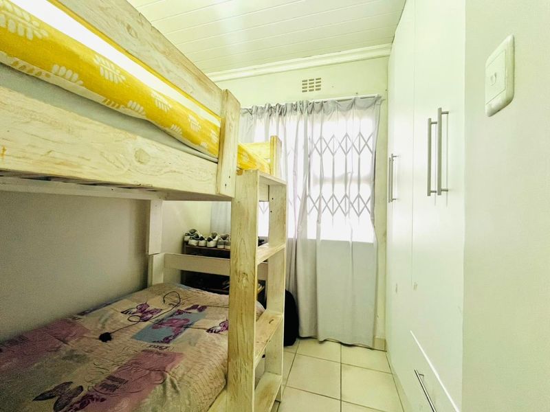 A compact bedroom featuring built-in cupboards, tiled flooring, and a secure window with a fitted security gate.