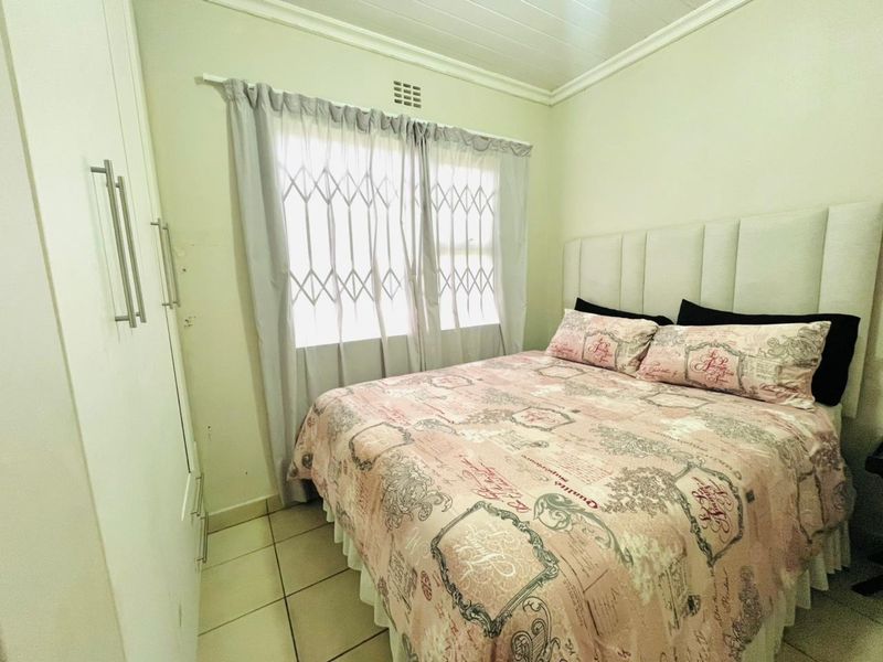 A functional bedroom featuring built-in cupboards, tiled flooring, and a window fitted with a security gate.