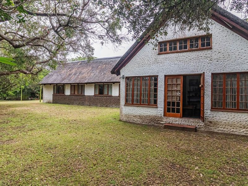 Rear view of a traditional thatched-roof house featuring textured stucco walls, brick detailing, and timber-framed windows overlooking a spacious garden area.