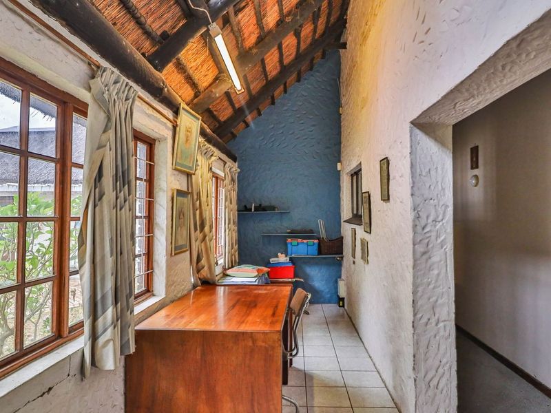 A rustic office space featuring a high-pitched thatched roof with exposed timber rafters, tiled flooring, and large timber-framed windows providing natural light.