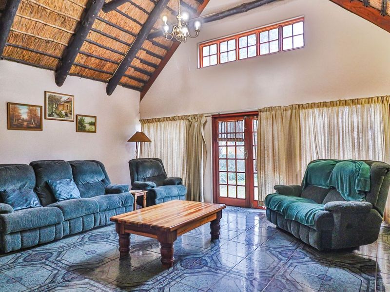 Spacious living room featuring a high vaulted thatched ceiling with exposed timber rafters, tiled flooring, and direct access to the outdoors via glass doors.