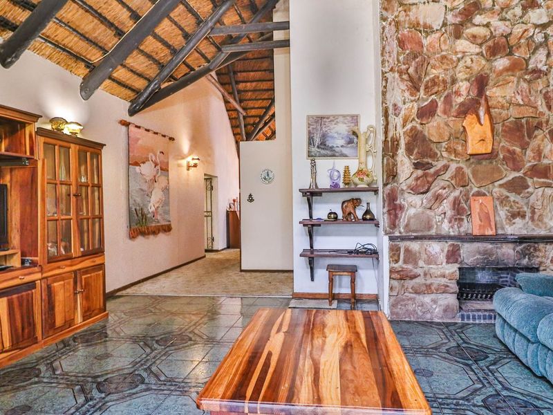 Spacious living room featuring a high vaulted thatched ceiling with exposed timber rafters, a prominent stone fireplace, and patterned tiled flooring.