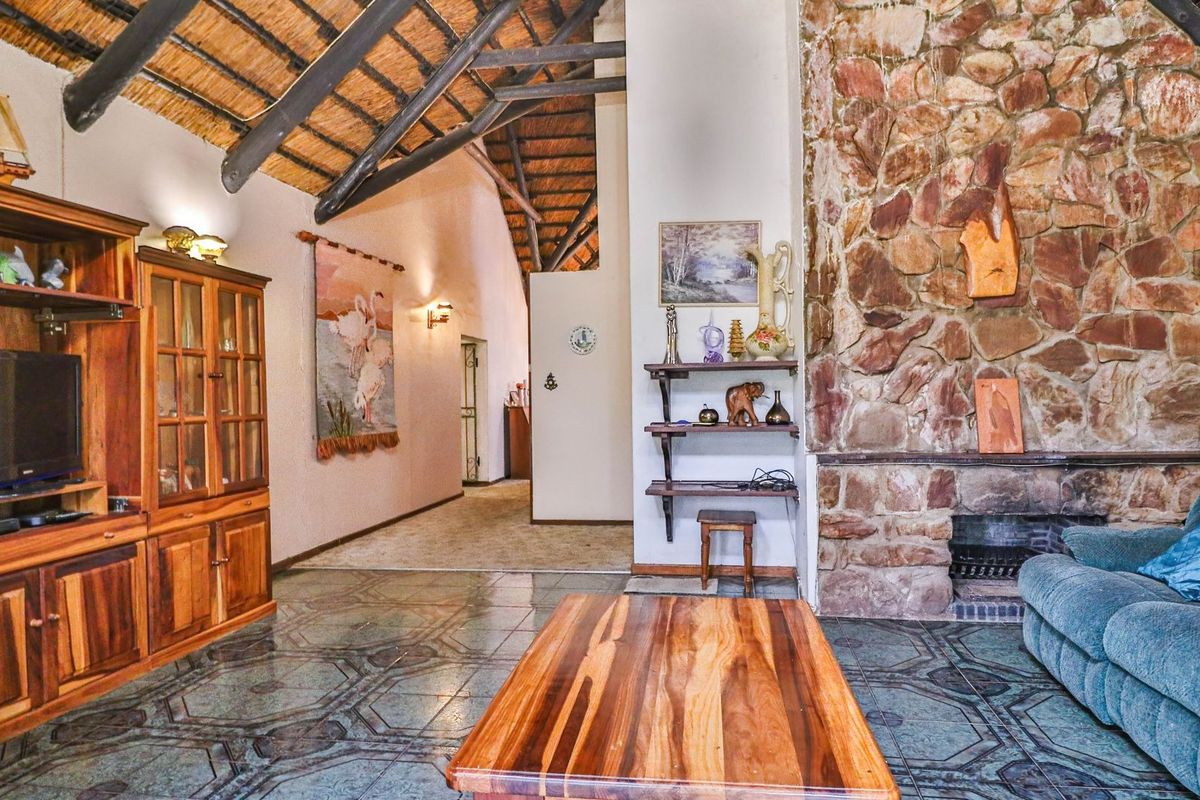 Spacious living room featuring a high vaulted thatched ceiling with exposed timber rafters, a prominent stone fireplace, and patterned tiled flooring.