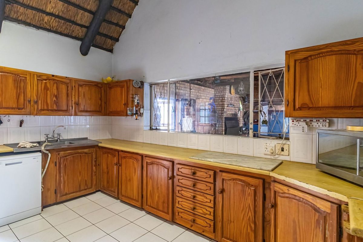 A dated kitchen featuring timber cabinetry, tiled splashbacks, and a distinctive high-pitched thatch roof ceiling, offering significant potential for a modern renovation.