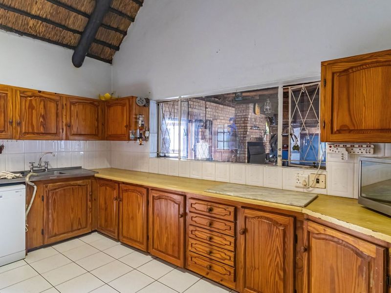 A dated kitchen featuring timber cabinetry, tiled splashbacks, and a distinctive high-pitched thatch roof ceiling, offering significant potential for a modern renovation.