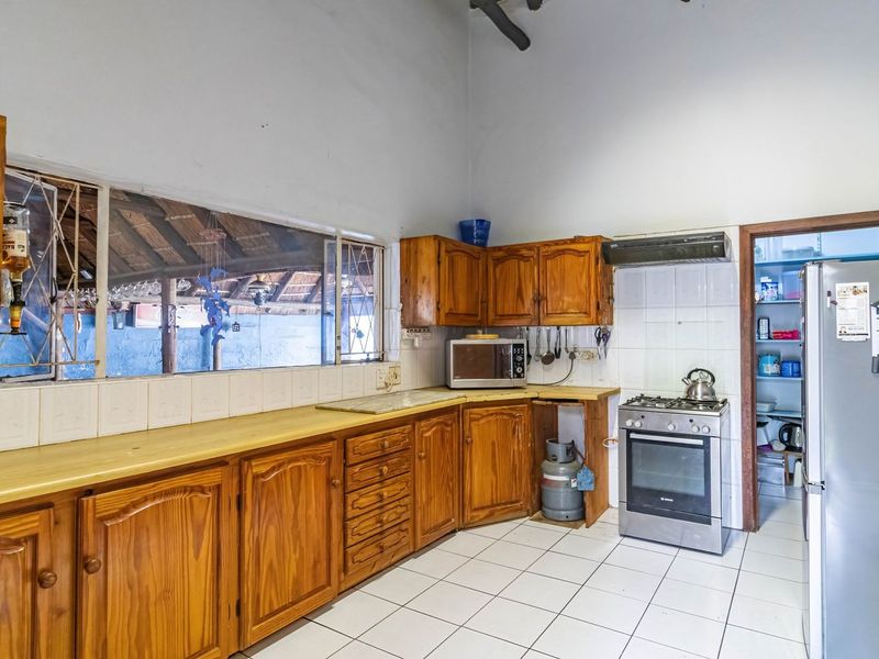 A functional kitchen featuring wooden cabinetry, tiled flooring, a gas stove with extractor fan, and a convenient adjoining scullery area.