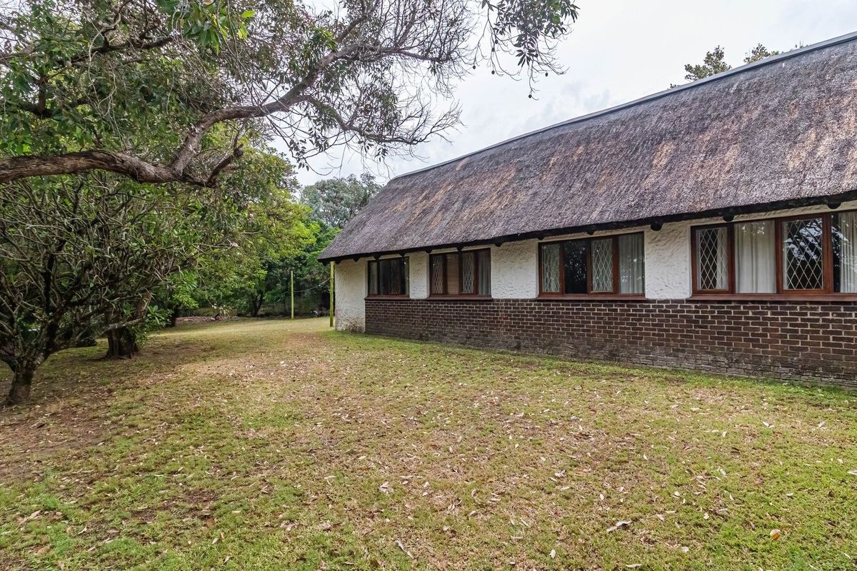 Rear view of a traditional house featuring a thatched roof, brick base, and leaded glass windows set within a spacious garden.
