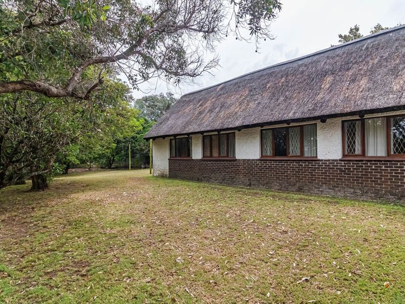 Rear view of a traditional house featuring a thatched roof, brick base, and leaded glass windows set within a spacious garden.