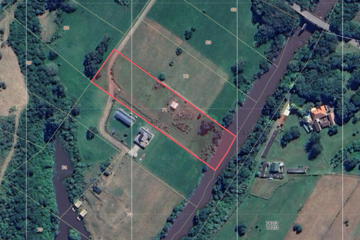 Aerial view of a vacant residential plot featuring river frontage and clearly marked property boundaries.