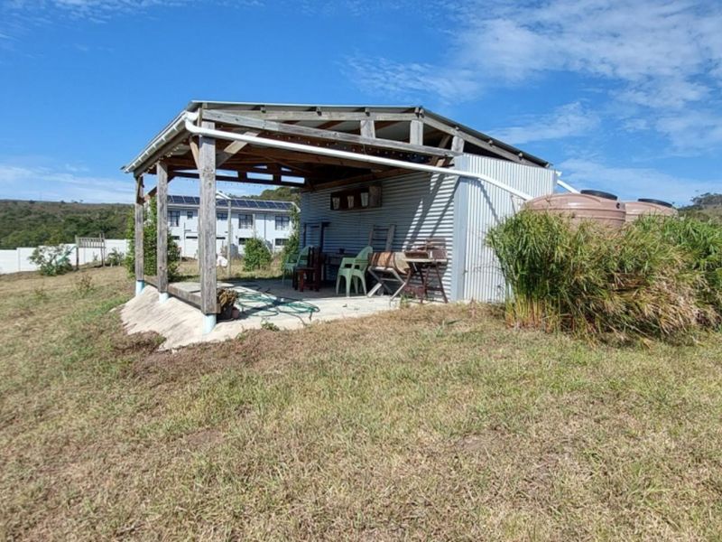 A rustic outdoor patio structure featuring a timber frame, corrugated metal siding, and integrated water storage tanks on a residential land plot.