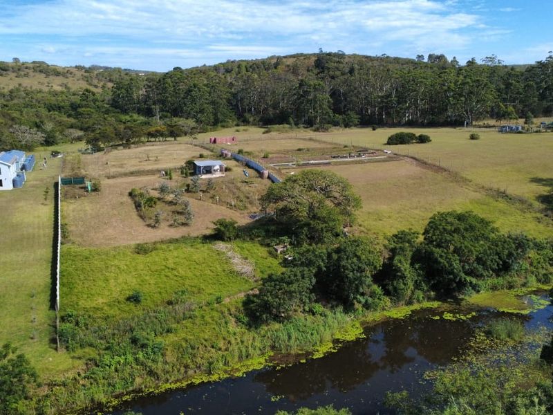 Aerial view of a large residential land parcel featuring open green space, mature trees, a water body, and existing residential structures.