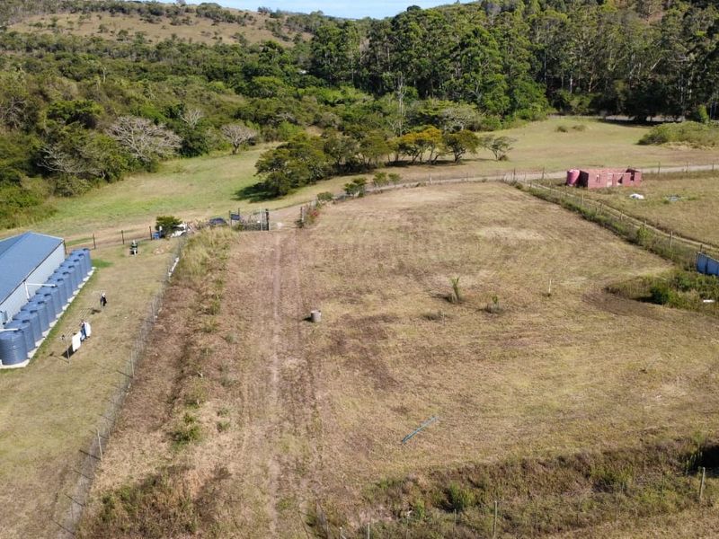 Aerial view of a vacant residential plot featuring perimeter fencing, a metal shed, and multiple water storage tanks on the property.