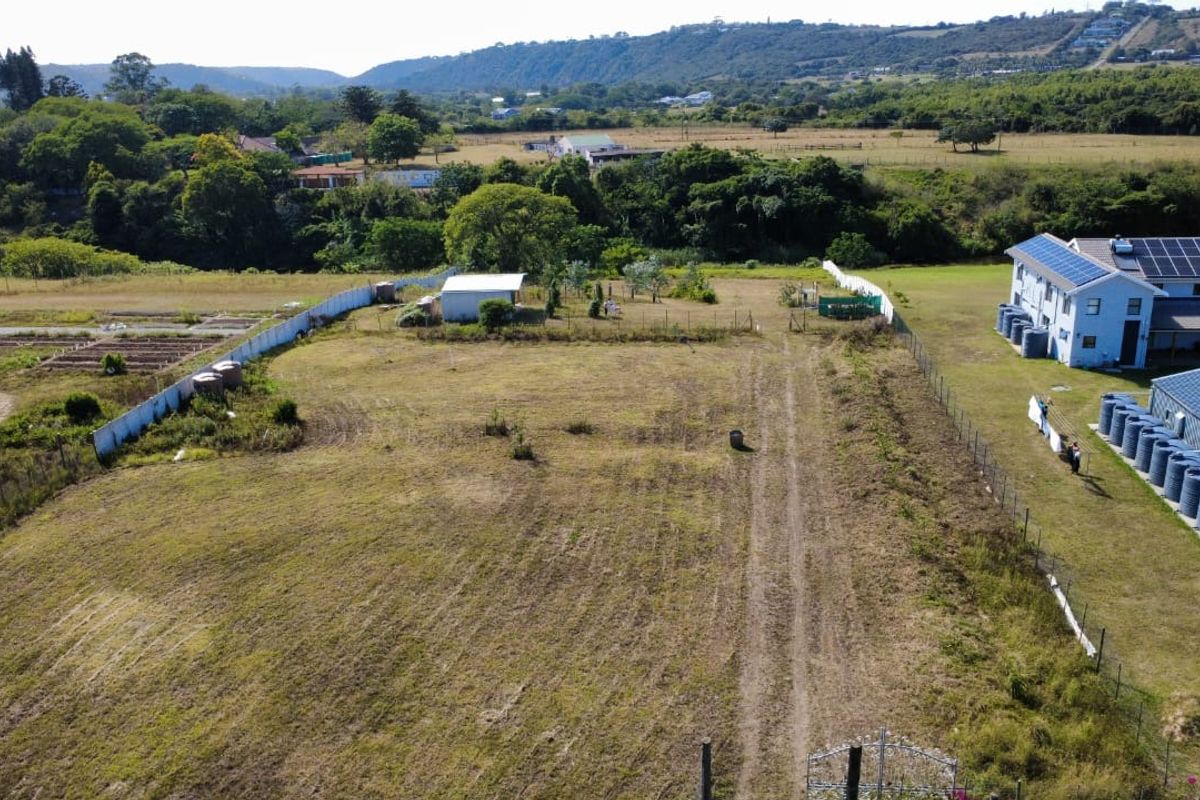 Aerial view of a vacant residential plot featuring perimeter fencing, water storage tanks, and an existing outbuilding set against a rural landscape.