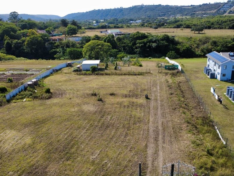 Aerial view of a vacant residential plot featuring perimeter fencing, water storage tanks, and an existing outbuilding set against a rural landscape.