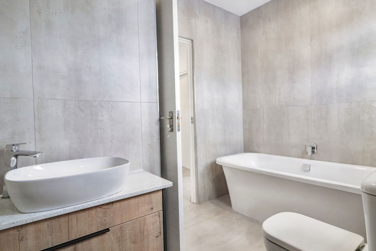 Modern bathroom featuring a sleek freestanding bathtub, contemporary vessel sink on a wood-finish vanity, and large-format neutral wall tiles.