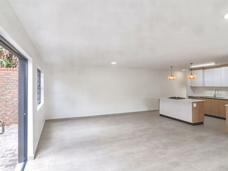 Spacious open-plan living and kitchen area featuring modern cabinetry, a central island with a gas hob, and large sliding doors leading to the patio.