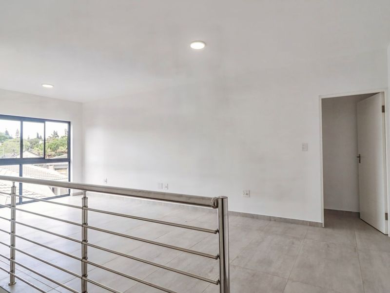 A bright, open-plan living area featuring modern tiled flooring, a sleek stainless steel balustrade, and large windows providing natural light.