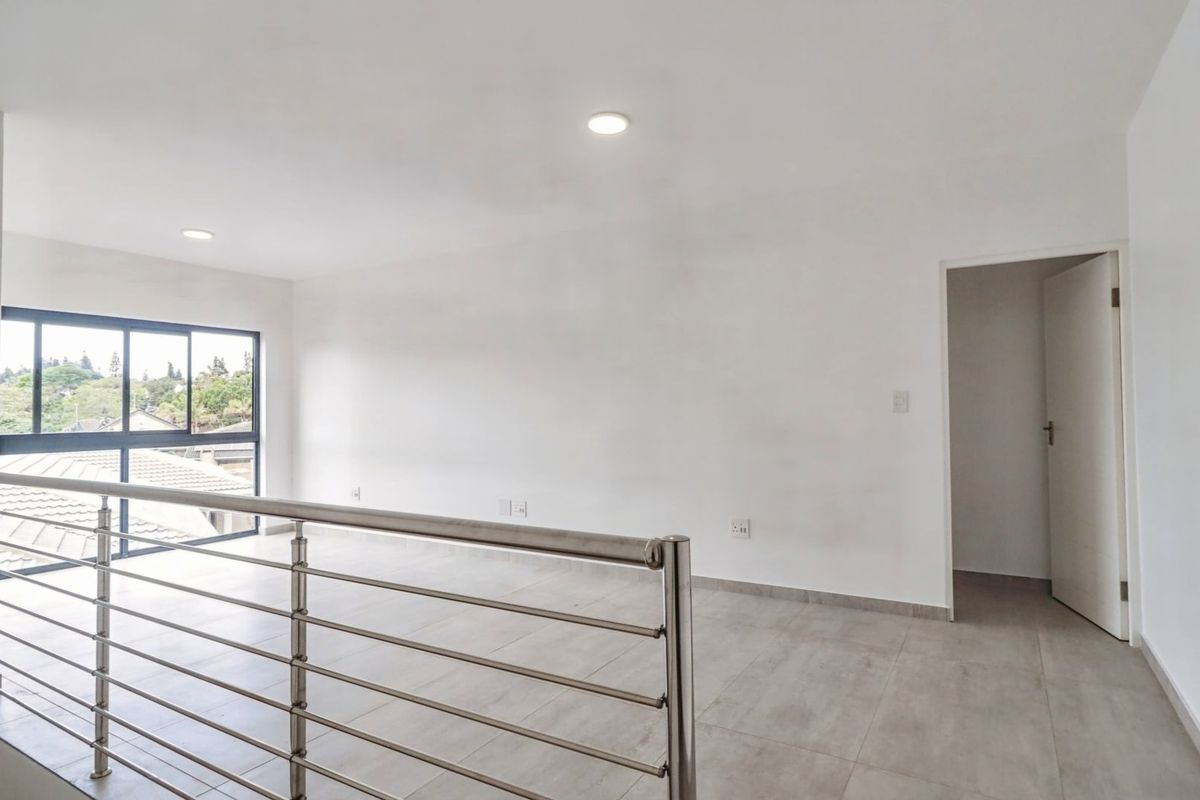 A bright, open-plan living area featuring modern tiled flooring, a sleek stainless steel balustrade, and large windows providing natural light.