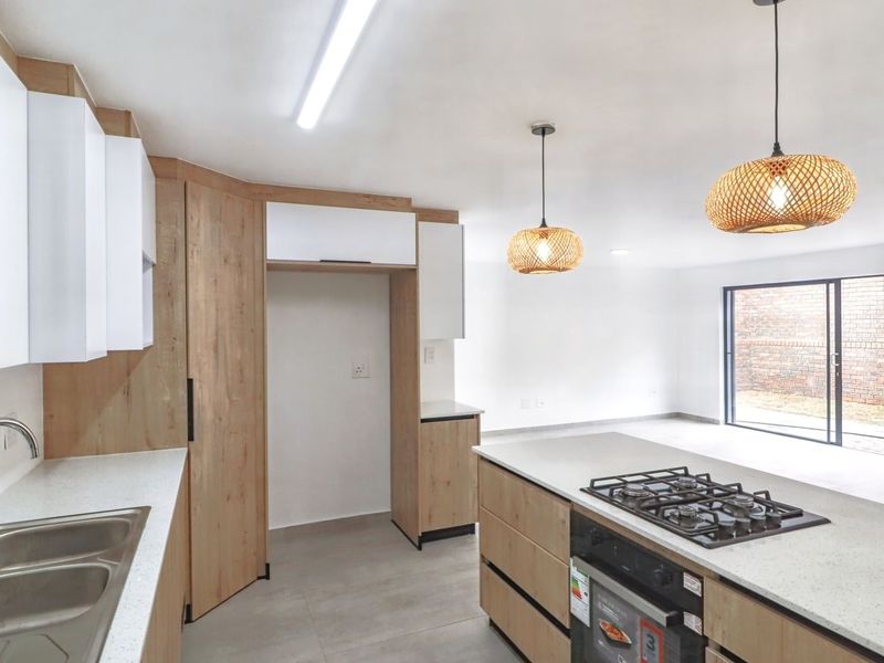 Modern open-plan kitchen featuring light wood and white cabinetry, stone countertops, gas hob, and seamless flow to the outdoor patio area.