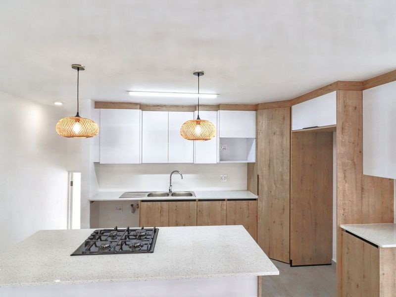 Modern kitchen featuring light wood and white cabinetry, stone countertops, a central island with a gas hob, and contemporary pendant lighting.