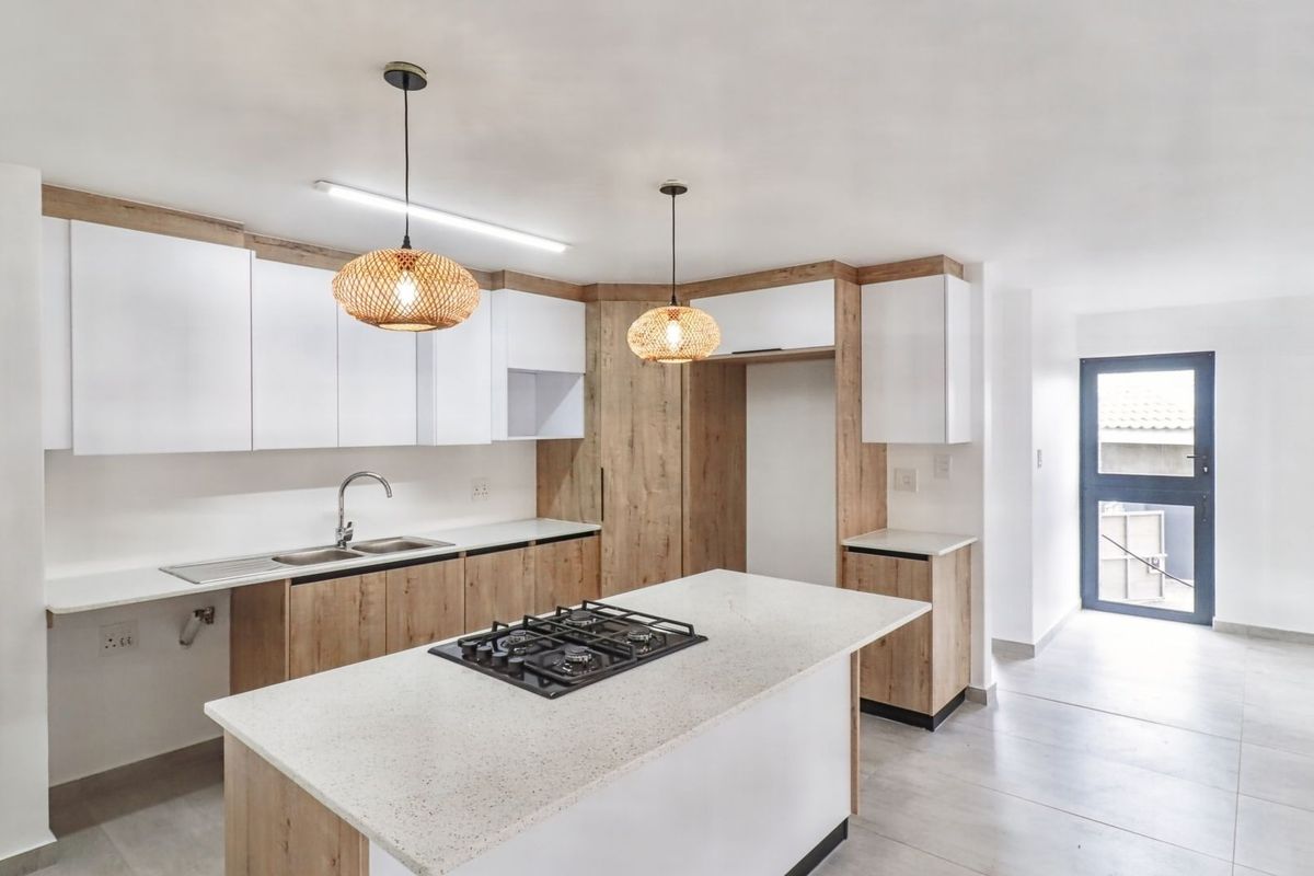 Modern kitchen featuring light wood and white cabinetry, stone countertops, a central island with a gas hob, and tiled flooring.