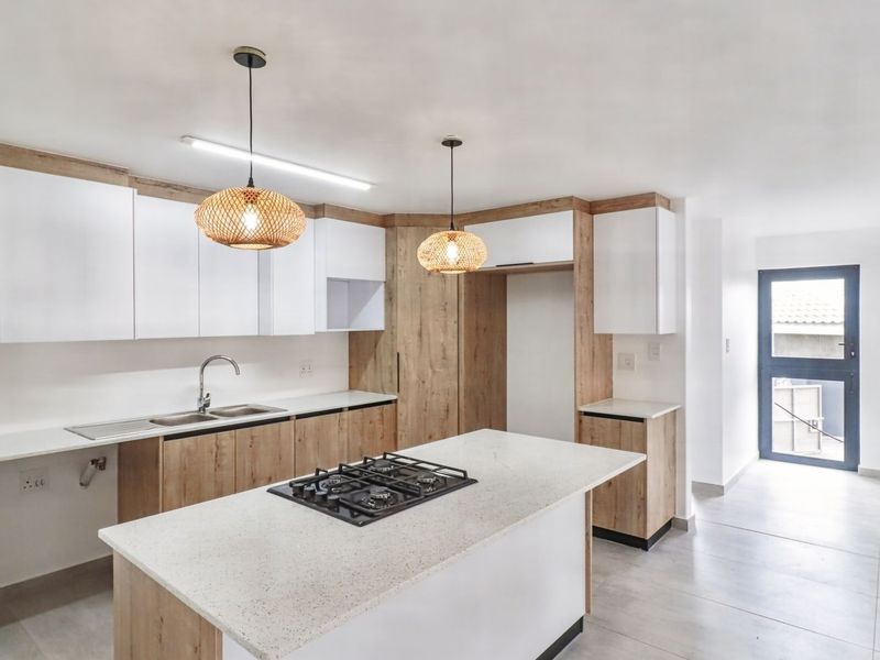 Modern kitchen featuring light wood and white cabinetry, stone countertops, a central island with a gas hob, and tiled flooring.