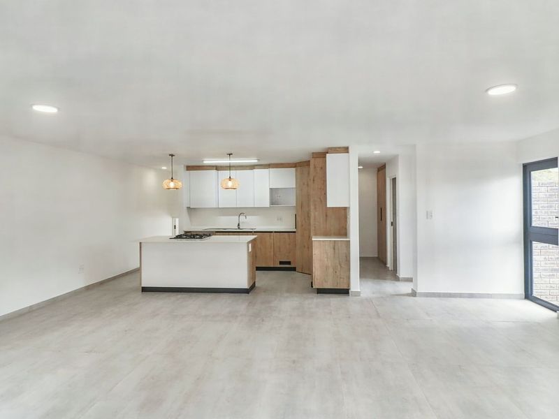 Spacious open-plan living area featuring a modern kitchen with a central island, gas hob, and neutral tiled flooring throughout.
