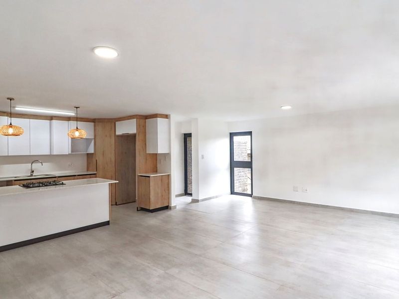 A bright, modern open-plan living and kitchen area featuring sleek cabinetry, stone countertops, a gas hob, and neutral tiled flooring throughout.