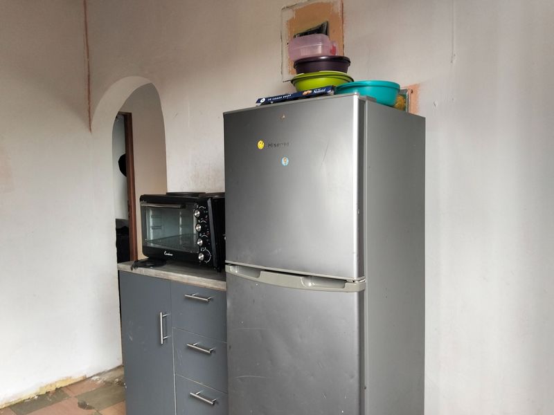 A small kitchen area featuring built-in grey cabinetry and a countertop, currently requiring wall finishing and repairs to the surrounding plaster and electrical points.