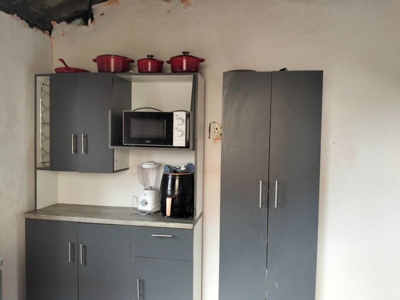 A kitchen area featuring dark grey built-in cabinetry and a laminate countertop, currently requiring wall and ceiling finishing to complete the space.