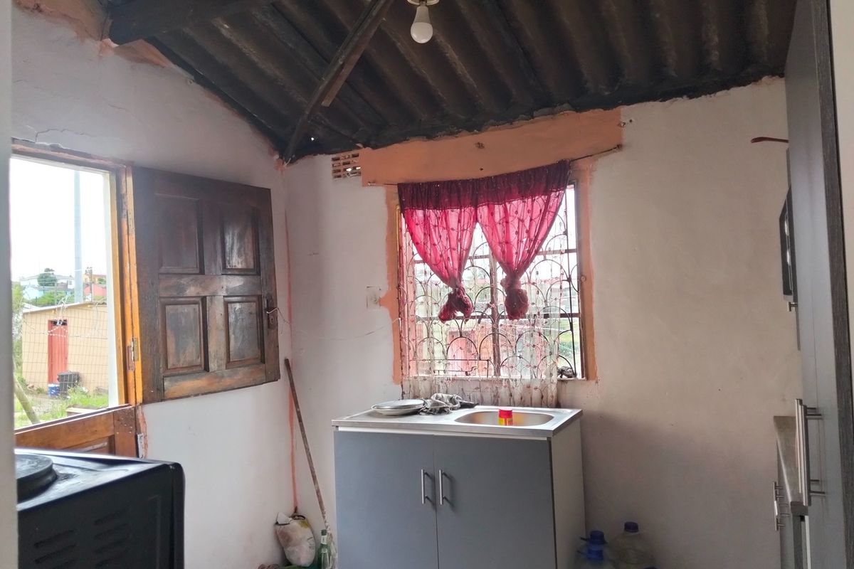 A compact kitchen area featuring a basic sink unit, exposed roof rafters, and direct access to the exterior through a timber door.