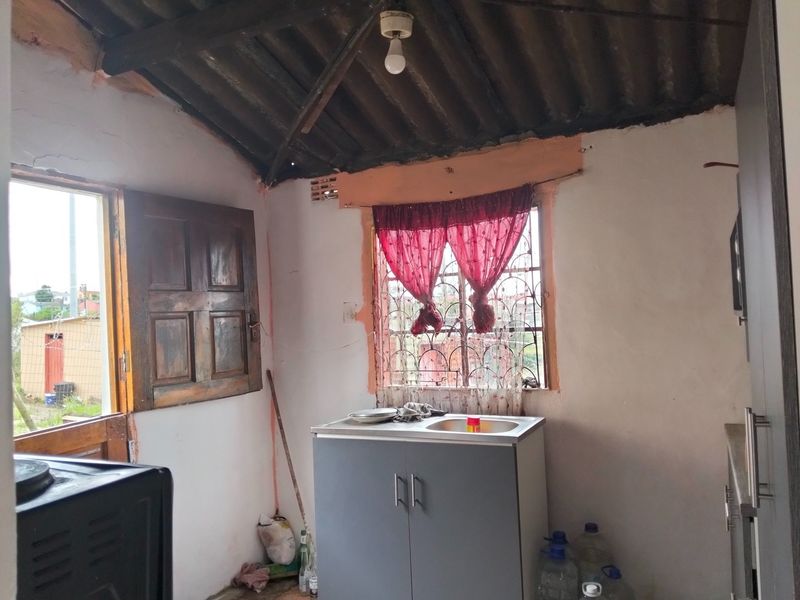 A compact kitchen area featuring a basic sink unit, exposed roof rafters, and direct access to the exterior through a timber door.