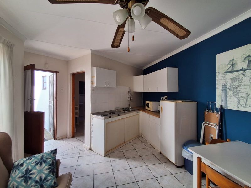 Open-plan living and kitchen area featuring tiled flooring, a ceiling fan, and functional built-in cabinetry with an integrated hob and sink.