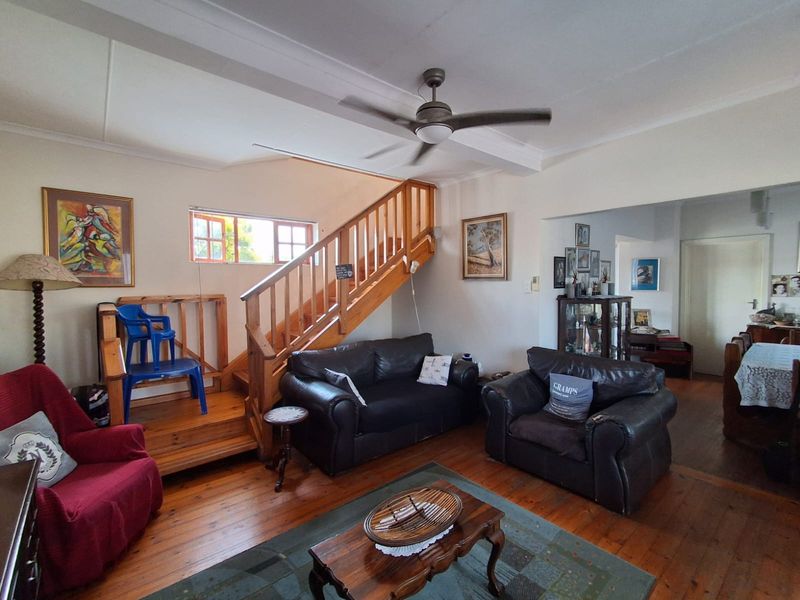 Spacious living room featuring polished timber flooring, a central timber staircase with balustrade, and a ceiling fan, offering a warm and traditional aesthetic.