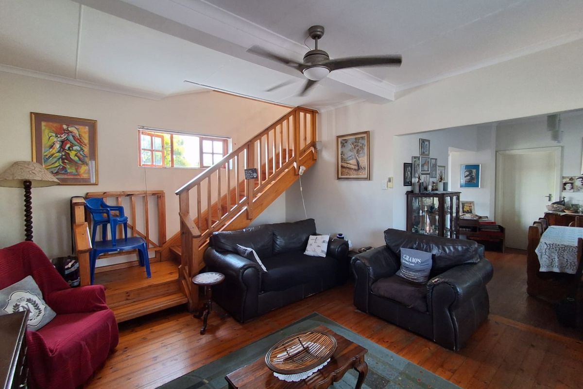 Spacious living room featuring polished timber flooring, a central timber staircase with balustrade, and a ceiling fan, offering a warm and traditional aesthetic.