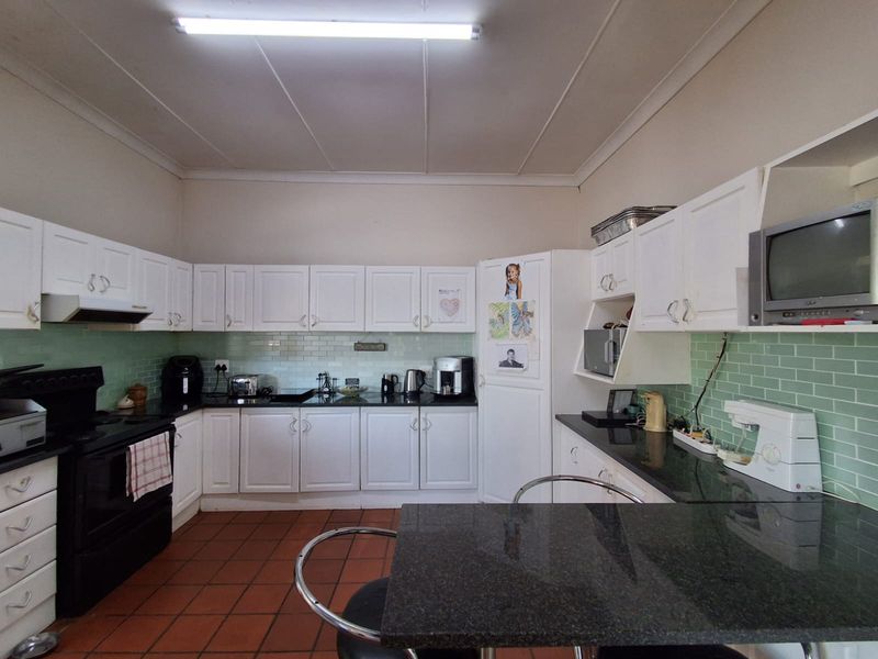 A functional kitchen featuring white cabinetry, black granite countertops, green subway tile backsplash, and terracotta flooring with an integrated breakfast bar.