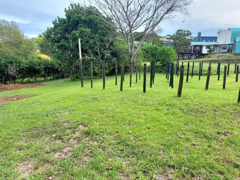 A vacant residential plot featuring a grassy landscape with multiple wooden support posts installed across the terrain.