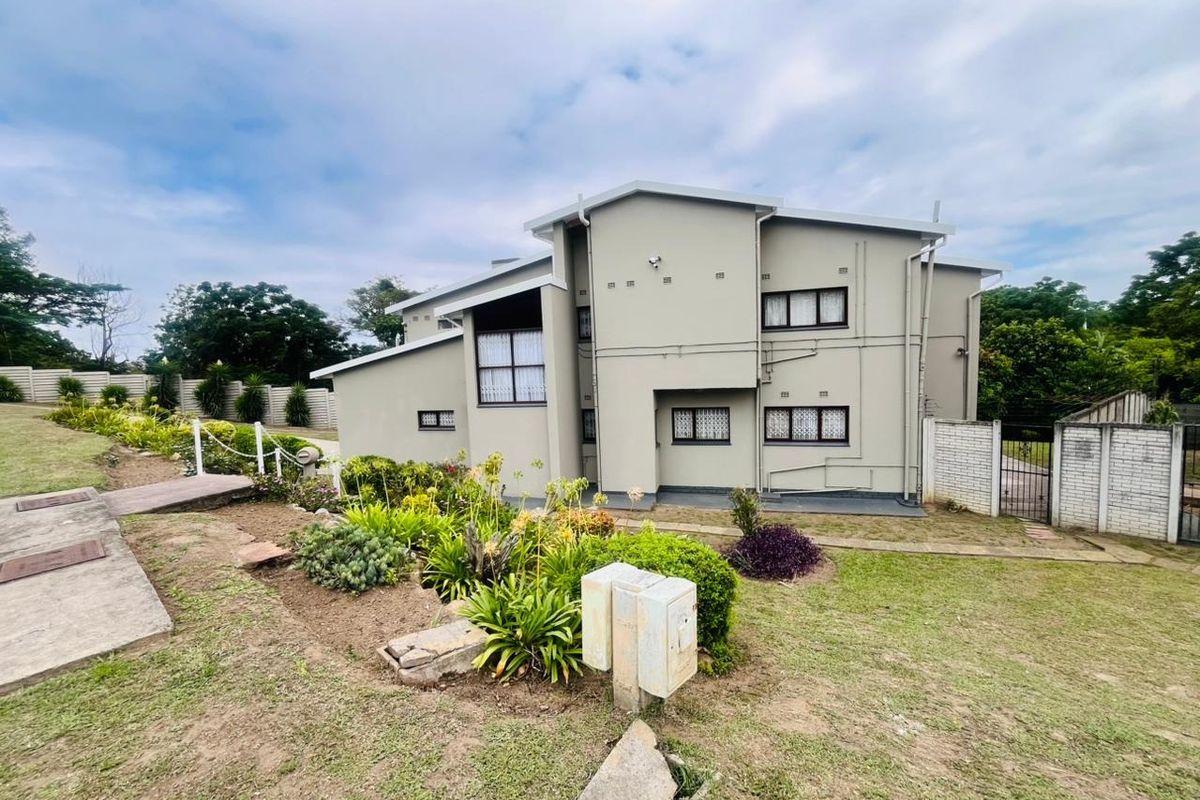 Rear view of a multi-level residential property featuring a landscaped garden, concrete pathways, and secure boundary walling.