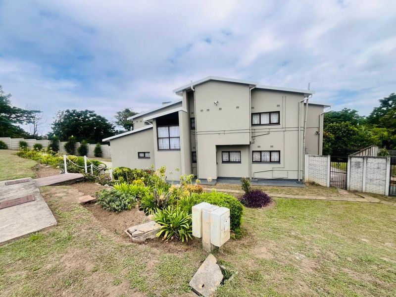 Rear view of a multi-level residential property featuring a landscaped garden, concrete pathways, and secure boundary walling.