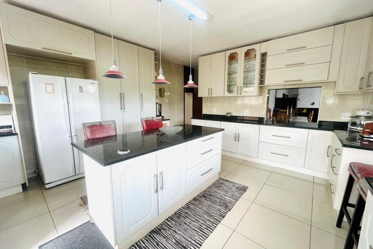 A functional kitchen featuring white cabinetry, granite countertops, a central island, and tiled flooring, offering a classic layout with ample storage space.