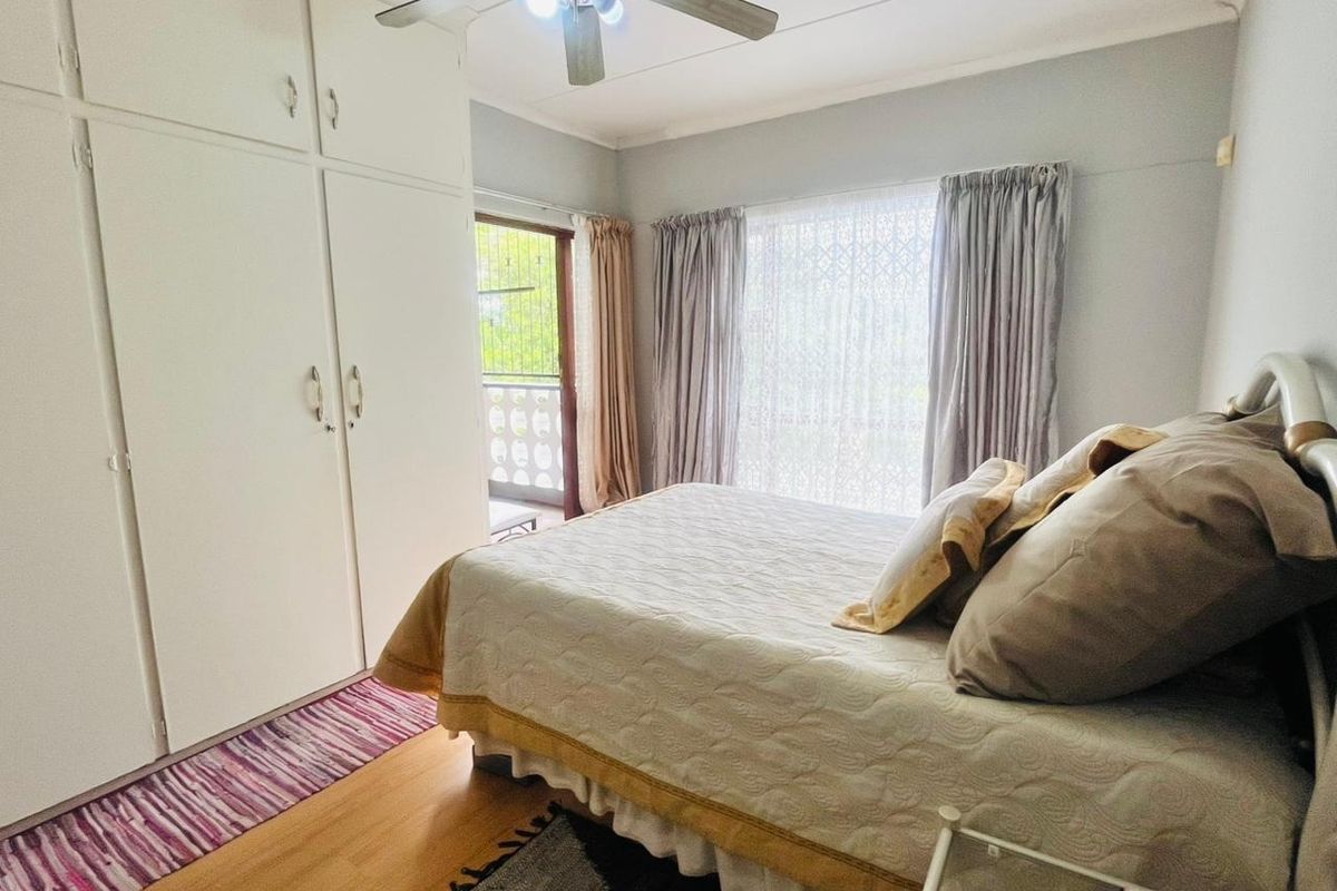A bedroom featuring built-in cupboards, laminate flooring, and a ceiling fan, with direct access to an outdoor balcony area.