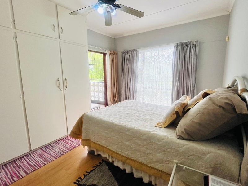 A bedroom featuring built-in cupboards, laminate flooring, and a ceiling fan, with direct access to an outdoor balcony area.