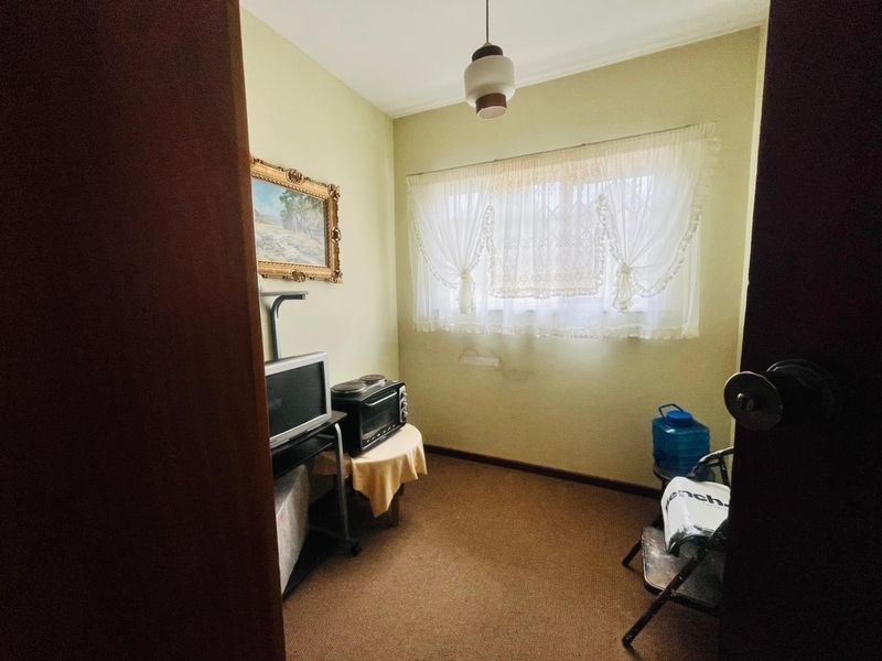 A small bedroom featuring carpet flooring, a pendant light, and a window with security bars, showing signs of wear on the wall.