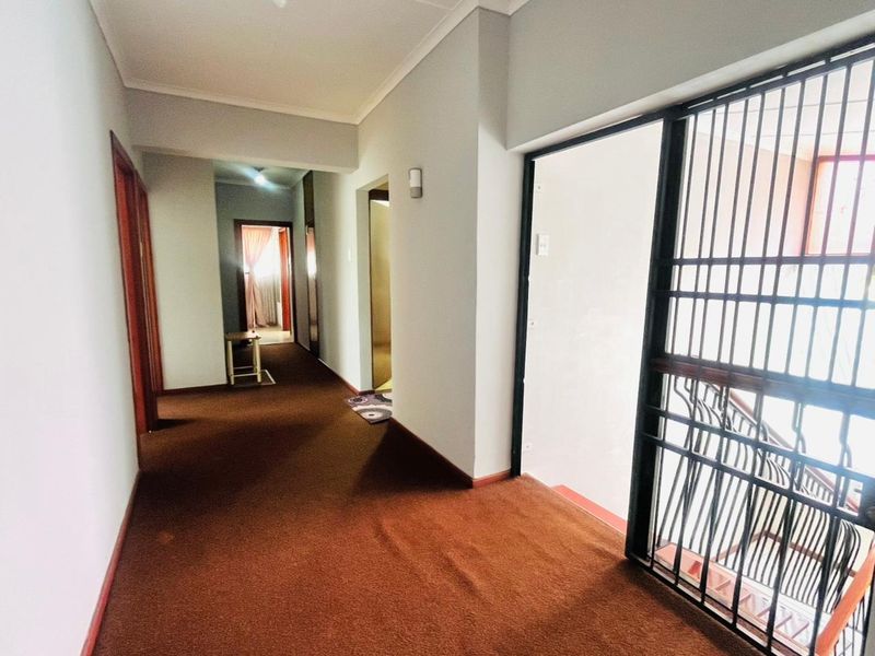 A spacious hallway featuring carpeted flooring and a secure metal gate leading to the staircase, providing access to multiple rooms.