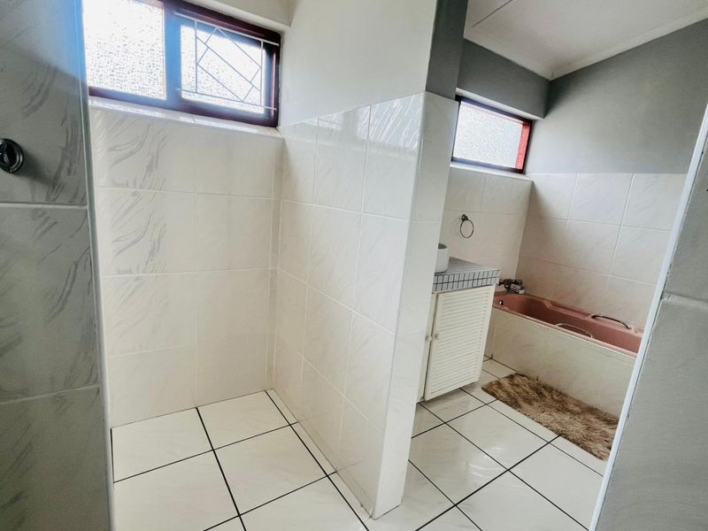 A functional bathroom featuring tiled walls and flooring, a built-in bathtub, and a vanity cabinet with obscured glass windows for privacy.