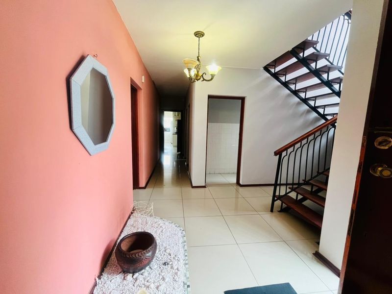 A spacious hallway featuring tiled flooring and an open-plan staircase with wooden treads and a wrought iron balustrade.