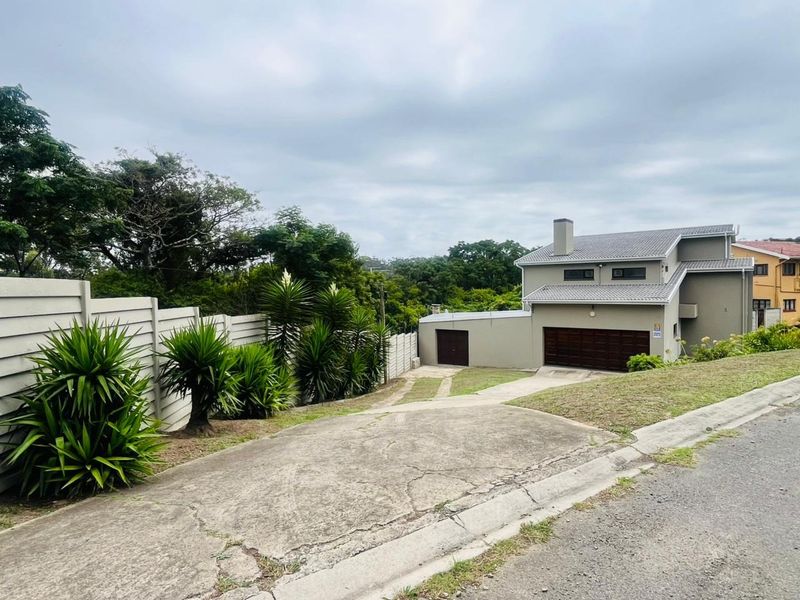 Front view of a multi-level residential property featuring a concrete driveway, garage, and perimeter boundary wall.